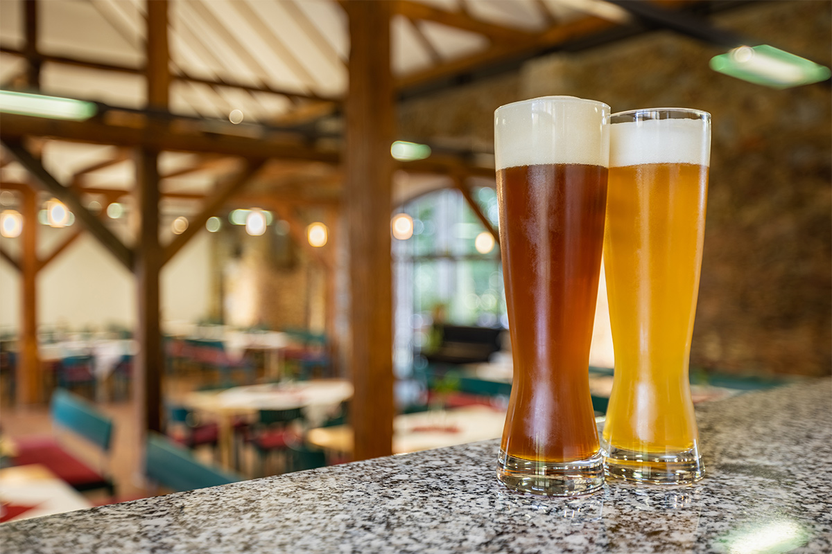 Zwei Radreisende stehen mit Biergläsern im Besucherbereich der Landskronbrauerei in Görlitz; im Hintergrund sind Bar und Backsteinwand zu sehen.