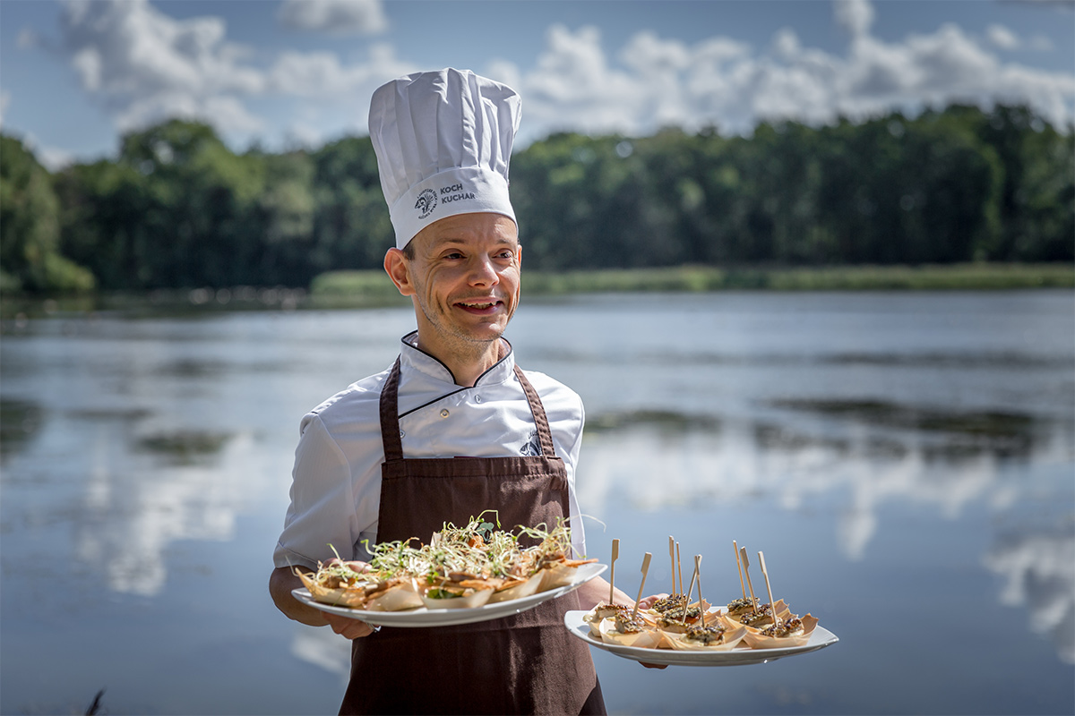 Ein Koch präsentiert angerichtete Fischhäppchen vor einem Teich in der Oberlausitzer Heide- und Teichlandschaft.