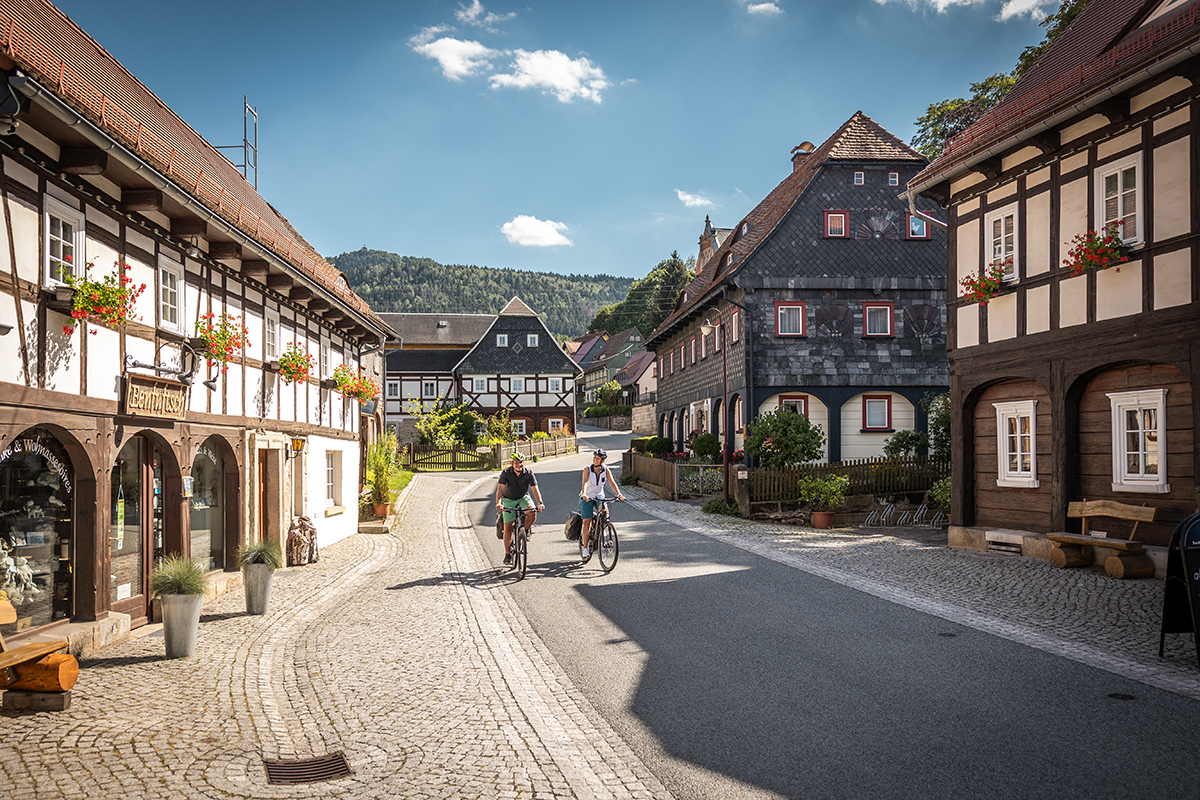 Luftaufnahme einer Oberlausitzer Ortschaft mit Kirche, Umgebindehäusern, grünen Gärten und sanfter Hügellandschaft.