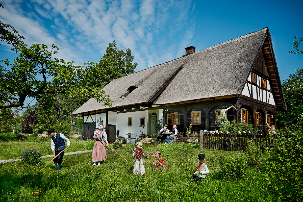 Historisch inszenierte ländliche Alltagsszene vor einem Oberlausitzer Umgebindehaus mit Menschen in traditioneller Kleidung.